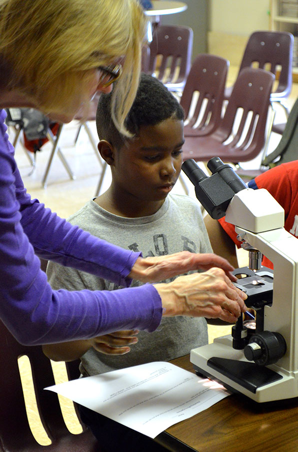 Scientist shows a grade school student how to operate a microscope